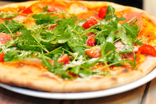 Frisch gebackene Pizza mit Rucola und Tomaten von Pizza Werk auf einem Teller